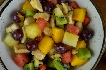 Refreshing fruit salad, natural colors, different textures and cuts, served in crockery container and small white plate, approximate photo
