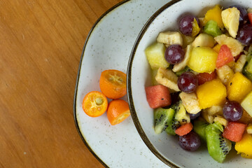refreshing fruit salad, natural colors served in crockery container and small white plate, decorated with small oranges, wooden background in top photo with space for text on the side
