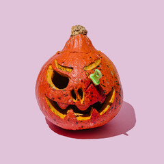 Scary Jack halloween pumpkin with a toy knife in his eye. Happy Halloween concept. Pink background