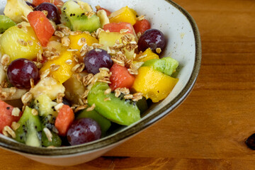 delicious fresh tropical fruit salad served in white container for afternoon snack, photo taken sideways on wooden background with space for text beside