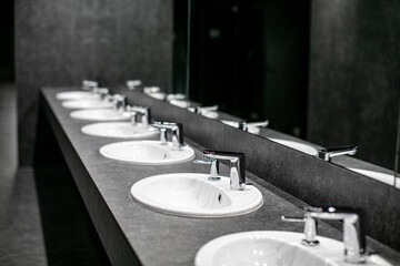 Faucets with washbasin in public restroom in gray colors