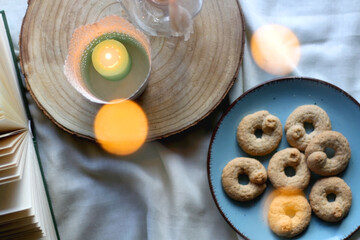 Plate with cookies, open book, lit candles and fairy lights. Hygge at home. Flat lay.