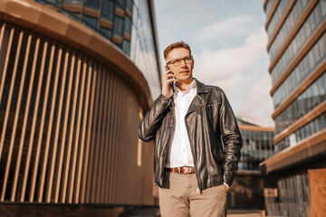 Handsome man with glasses with a smartphone on the street of a big city. Businessman talking on the phone on urban background