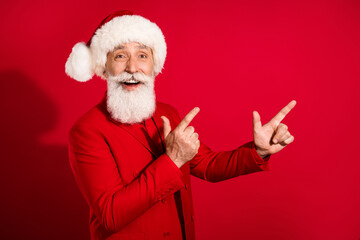 Photo of charming cute mature man dressed christmas costume hat pointing fingers empty space isolated red color background