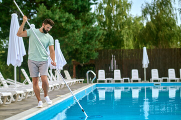 Fototapeta na wymiar A service person cleaning the swimming pool and looking busy