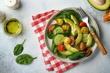 Avocado, red, yellow, black cherry tomato, spinach and cucumber fresh salad with spices pepper and olive oil in grey bowl on grey slate, stone or concrete background. Healthy food concept. Top view.