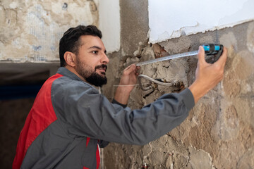 Plumber with tape measure measures the distance between pipes to avoid puncturing them when drilling