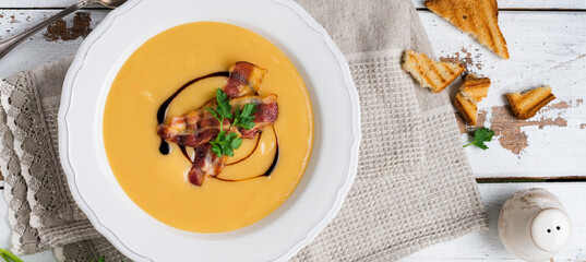 Potato soup cream with bacon and soy sauce in white bowl, on light old wooden background. Top view