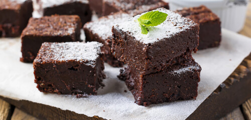 Chocolate brownies with powdered sugar and cherries on a dark wooden background. Selective focus.