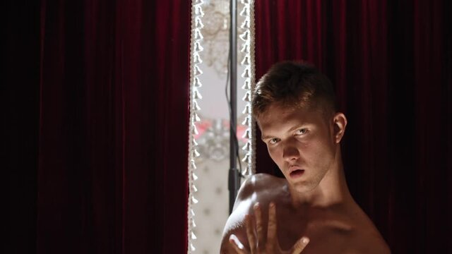 Young shirtless man stripper performing bizarre dancing in contrast lighting - looking in the camera