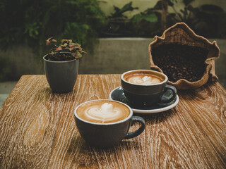 Two cups of cappuccino with latte art on wooden table surface background and coffee beans. Beautiful foam, ceramic cups.