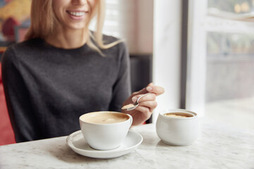 Young woman putting sugar in cup with cappuccino