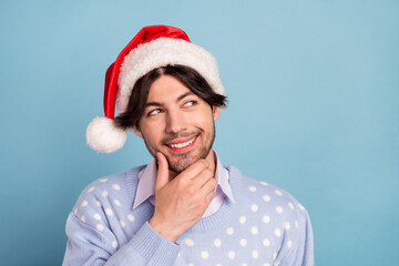 Photo of positive young dreamy minded man look empty space wear hat santa claus isolated on blue...