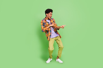 Fototapeta na wymiar Photo of sweet cute dark skin man wear plaid shirt smiling dancing pointing fingers empty space isolated green color background