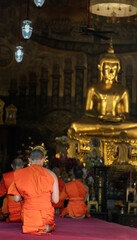 Obraz premium Bangkok, Thailand - Nov 15, 2020 : Buddhist monks sitting praying and pay respect Buddha image in main vihan. Evening Chant. Focus and blur.