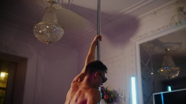 Young shirtless man stripper bizarre dancing by the pole in the studio