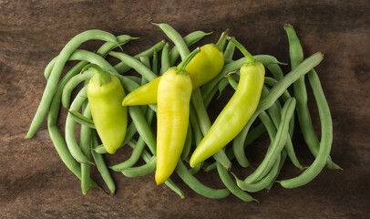 bunch of green beans with green chili peppers on a wooden surface, closeup view taken from above