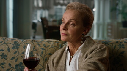 Portrait pensive elderly woman enjoying red wine glass at home. Old aged lady