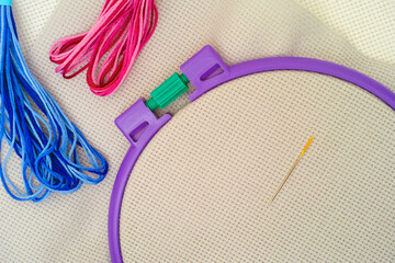 Cross stitch fabric in plastic embroidery hoop with needle, red and blue threads.