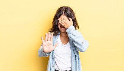 young pretty girl covering face with hand and putting other hand up front to stop camera, refusing...