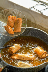 A chef is frying spring rolls in a pan