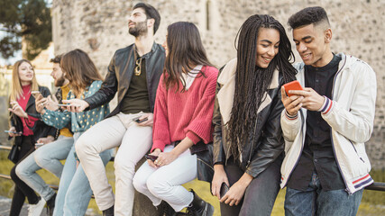 young friends watching viral social media video on mobile cell phone outdoors - Young adult friends using smartphones together -outdoors youth culture concept.