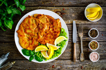 Breaded fried pork chop with lemon and fresh vegetables on wooden table
