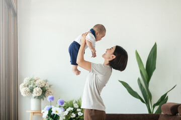 Happiness Asian mom playing with her son newborn in living room stay at home. Asian woman holding...