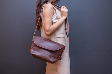 Woman carries brown leather messenger bag in the hand