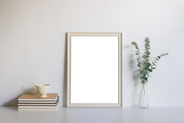 A blank picture frame with leaves and books on table.