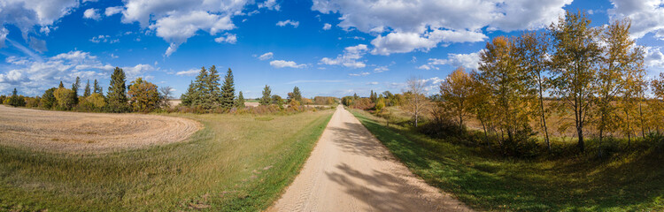 Fototapeta na wymiar Panoramic view along a country road with autumn colors in the trees and harvested farm fields. 