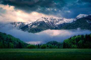 Mountain lit by the last light with a meadow, forest and spectacular cloud formations