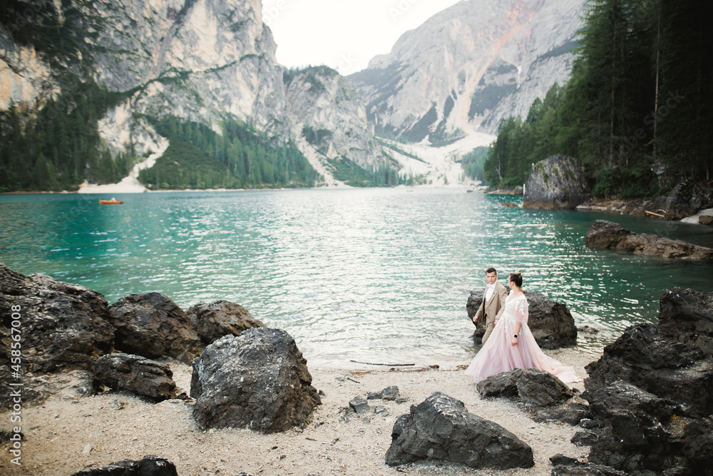 Wall mural Young couple near lake Karersee, Italy. Holding hands at the stone at lake