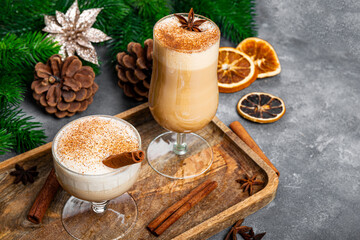  Two glasses of traditional Christmas drink eggnog on a gray background. Spicy drink made from egg and milk with cinnamon, cardamom.