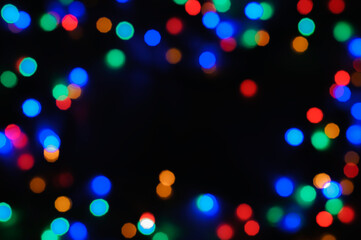 Bokeh, defocused colored lights forming a frame on a black background. Abstract festive background with copy space
