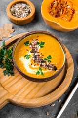 A bowl of homemade pumpkin soup with seeds, sesame seeds and flax seeds close-up, warm autumn food vertical photo