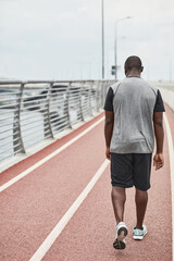 Rear view of African sportsman in sports clothing walking along the stadium after training