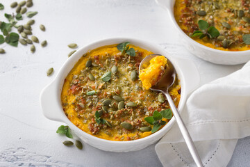 Homemade pumpkin casserole or gratin with cheese and pumpkin seeds in two ceramic tins on a light gray background