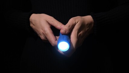 Hand with a led flashlight shining in the darkness with blue beam into the camera, spy and investigation concept