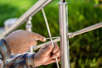A worker in gloves repairs a metal railing of a staircase using a screwdriver and a drill