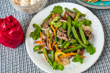 Plate with fried beef, green bean, carrot and onion, rice and small red bamboo box.