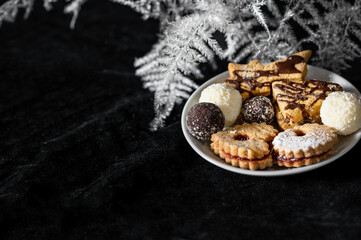 Christmas cookies on white plate on black velvet background with white bracken twi