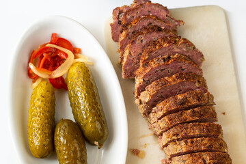 Sliced baked meatloaf on kitchen board, pickled cucumber with vegetatble.