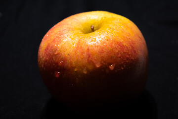Red and yellow apple with water droplets and black background
