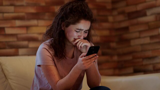 Beautiful teenager lady start crying in her bedroom while looking through the smartphone