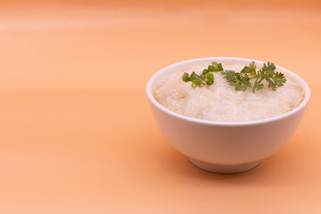 Rice porridge There are condiments on top in white bowls on the side view. Orang background