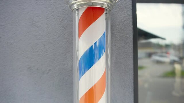 Barber pole on wall in hairdresser shop. Barber pole spinning at barbershop. Vintage barbershop and hairdresser symbol. Traditional barber pole in barbershop