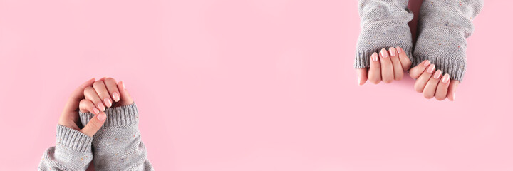 Female hands in gray knitted sweater with beautiful manicure - pink nude nails on pink background, wide panoramic banner with copy space. Nail care concept