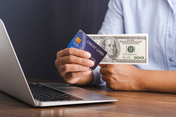 Close-up of hand holding a credit card and dollar banknotes for shopping online with a laptop. Business, e-commerce, and payment concept