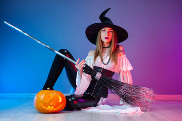 a girl in a witch costume for Halloween with a broom and a pumpkin in neon light